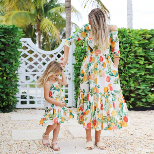 Two women in matching floral dresses standing outdoors with greenery and a white lattice structure in the background.