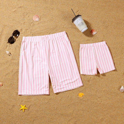 Pink and white striped shorts on a sandy surface with sunglasses and a cup.