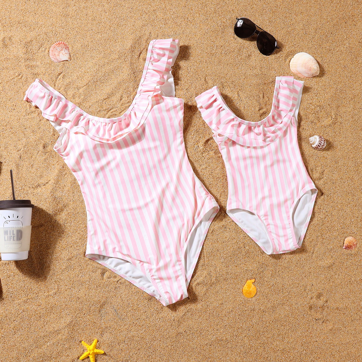 Pink and white striped swimsuits on a sandy surface with shells and sunglasses.