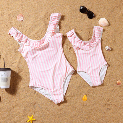 Pink and white striped swimsuits on a sandy surface with shells and sunglasses.