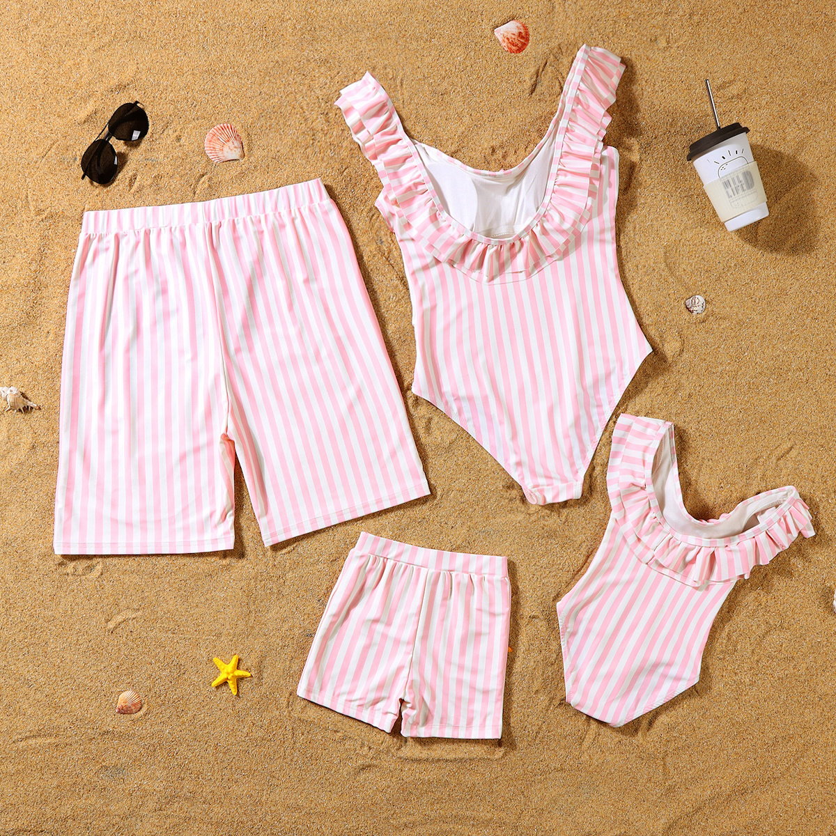 Pink and white striped swimsuits and shorts on a sandy surface with beach accessories.