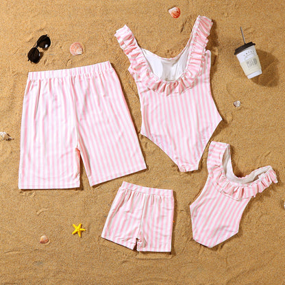 Pink and white striped swimsuits and shorts on a sandy surface with beach accessories.