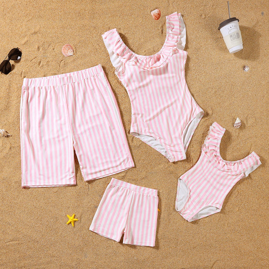 Pink striped swimsuits and shorts on a sandy surface with beach accessories.