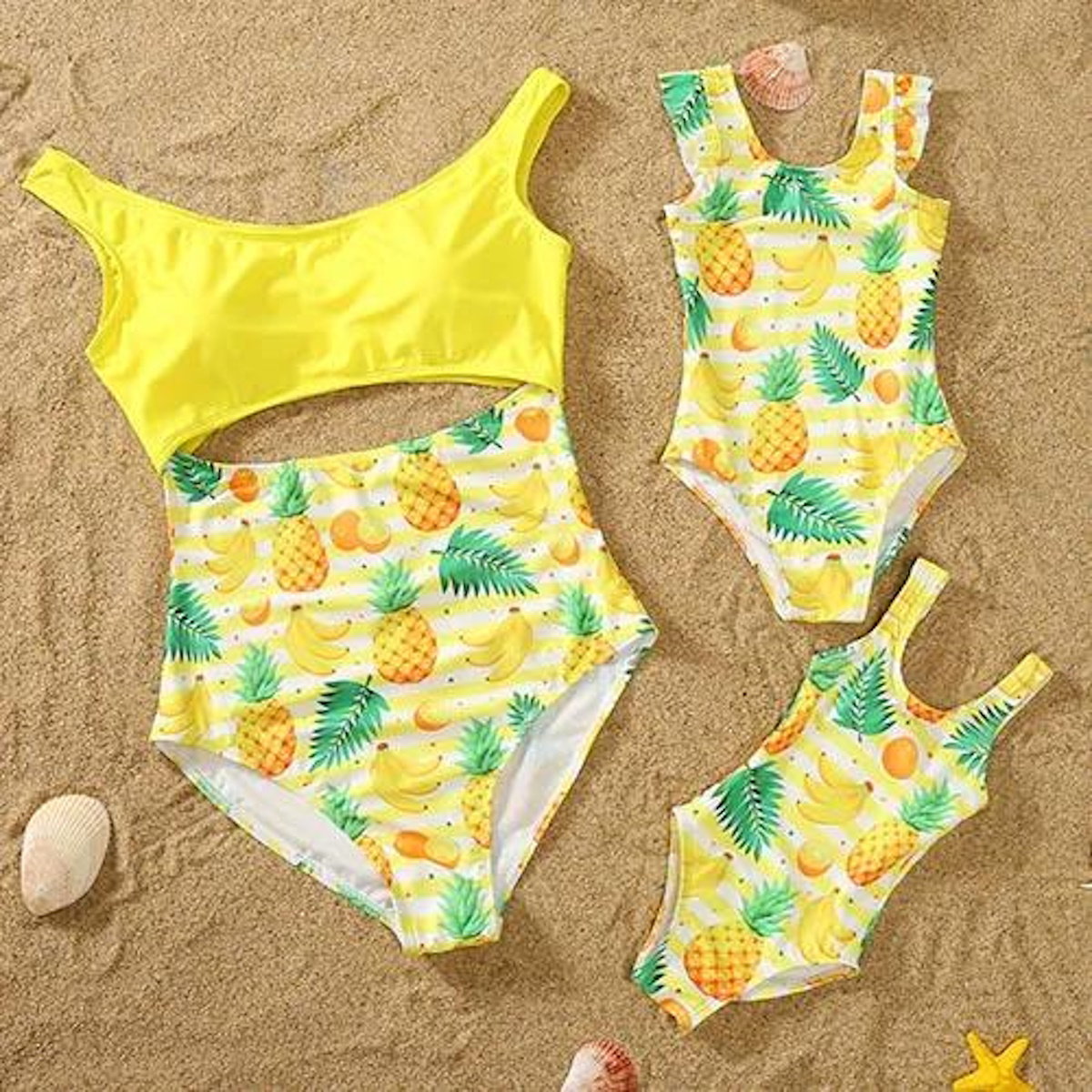 Set of yellow swimsuits with pineapple and fruit pattern on a sandy background