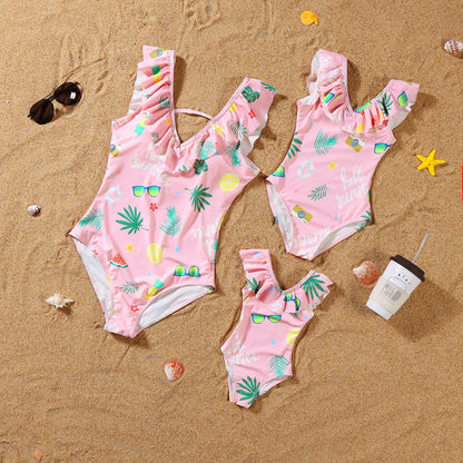 Three pink children's swimsuits with tropical patterns on a sandy surface.