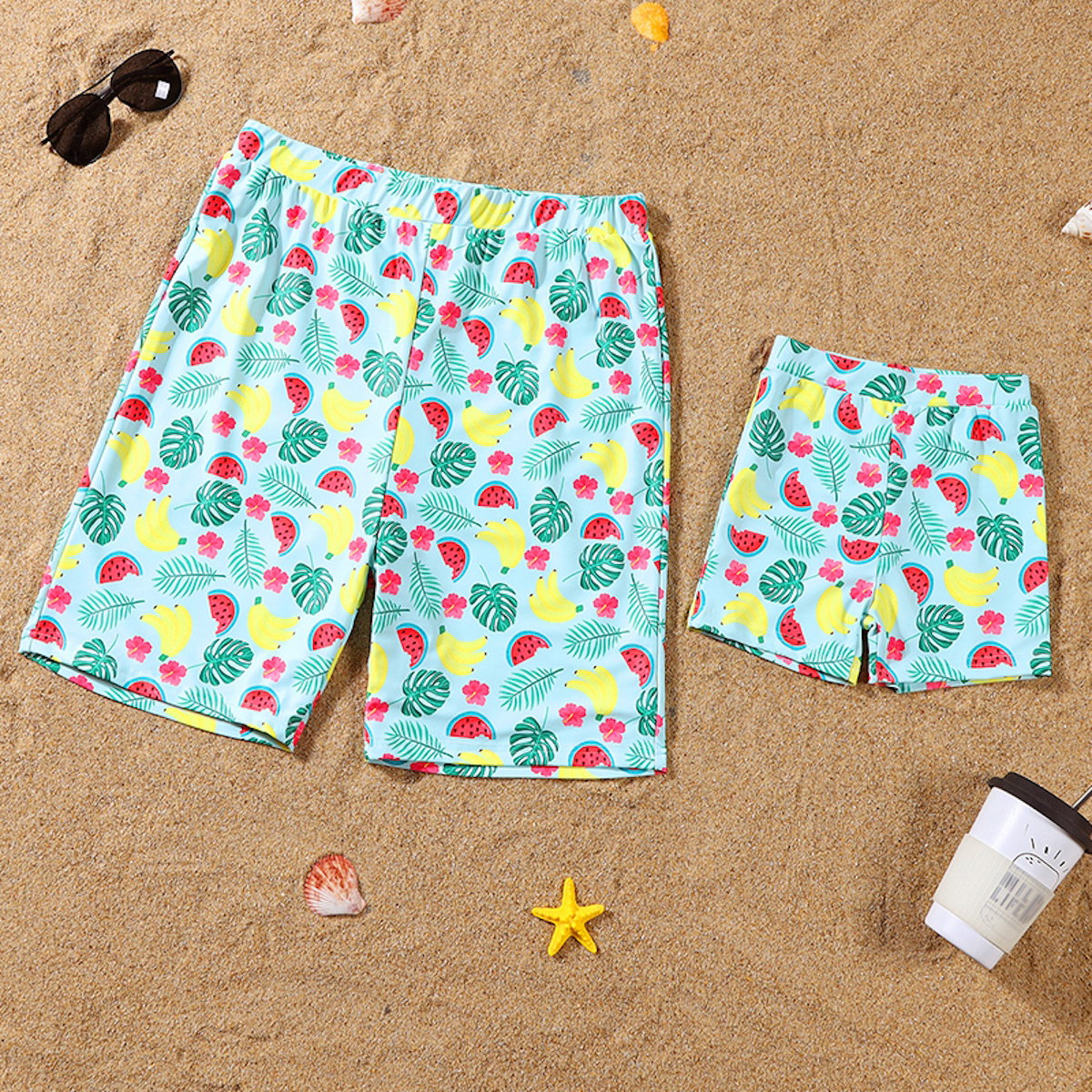 Fruit-patterned shorts on a sandy surface with beach accessories.