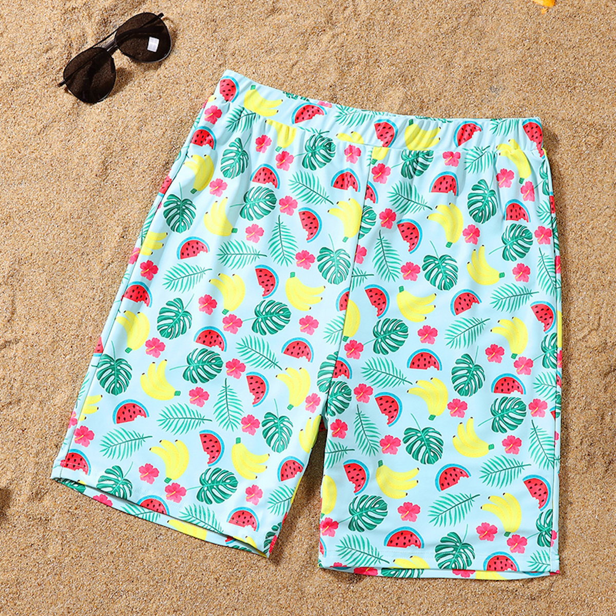Colorful patterned shorts on a sandy surface with sunglasses.